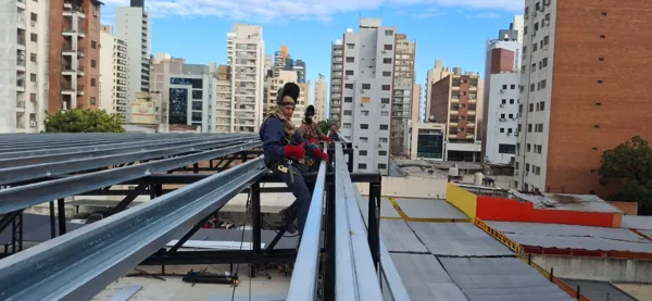 Dos soldadores trabajando sobre la estructura de un techo en una terraza rodeada de edificios